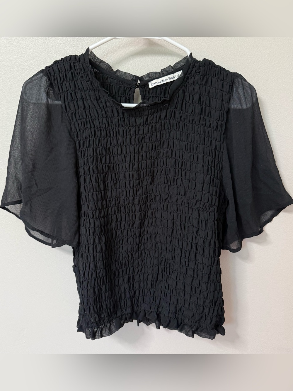 No tears or stains. Smocked body with sheer flutter sleeves. Stretchy. Keyhole b